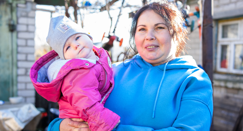 A woman holds her children in Kherson, Ukraine, after receiving a gas stove from the IRC to help warm their flood damaged house through winter. 