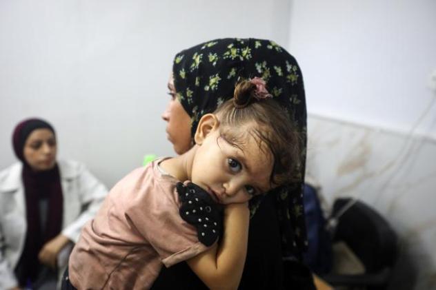 A woman leads a young child by the hand through the rubble of destroyed buildings.