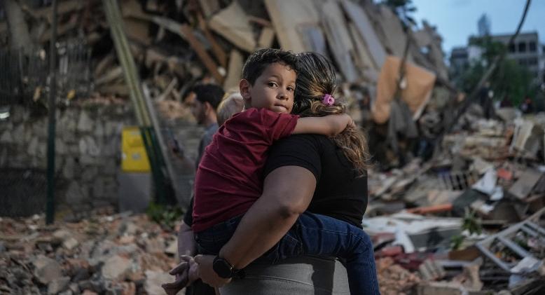A person carries a child in front of a pile of rubble and destroyed buildings after an earthquake in Venezuela.