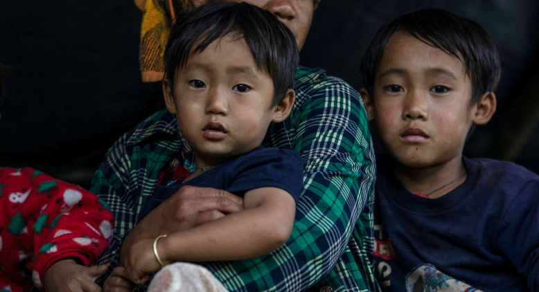 A displaced mother holds two of her young children on her lap in Myanmar. 