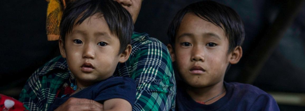 A displaced mother holds two of her young children on her lap in Myanmar. 