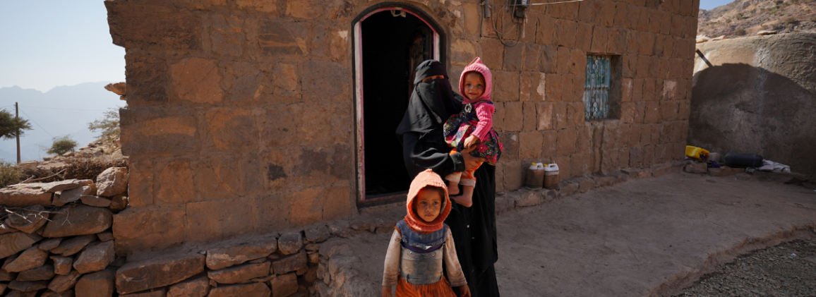 A woman with two young children outside a stone dwelling in Al-Khirbet Village, Jahaf, Yemen.